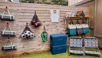 A &ldquo;Surf Land&rdquo; gear shed wall stocked with beach sports items&mdash;balls, bags, coolers, and surf towels&mdash;hung on a wooden backdrop.