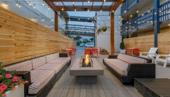 Outdoor patio with string lights, red chairs, and a central stone fire pit between cozy bench seating.