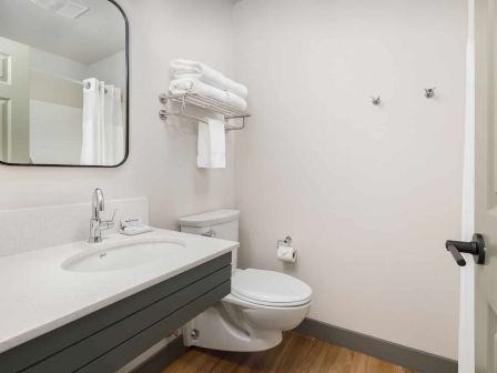 Clean modern bathroom with white toilet, sink, towel rack, mirror, and light switches on a bright wall.