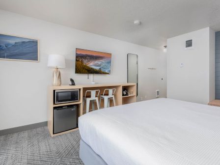 A modern hotel room with a large bed, kitchenette with microwave and fridge, and ocean/mountain wall art.