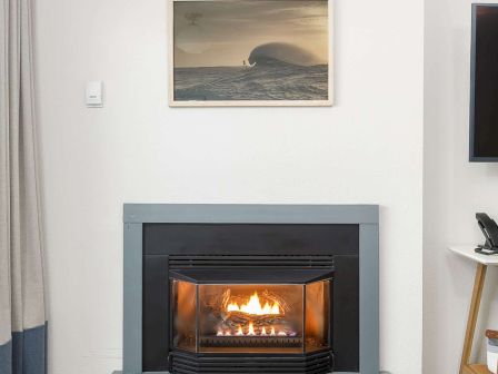 A cozy living room with a lit fireplace, framed ocean artwork, a flat-screen TV, and patterned carpet.