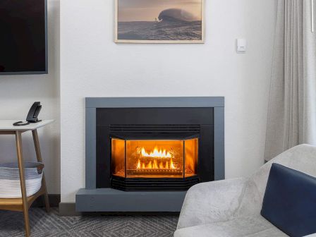 A cozy living room with a lit fireplace, a framed ocean artwork, a small phone by a side table, and a light gray sofa.