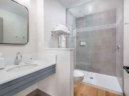 A modern bathroom with a white vanity and sink, a bathtub with glass shower, toilet, and towel racks.