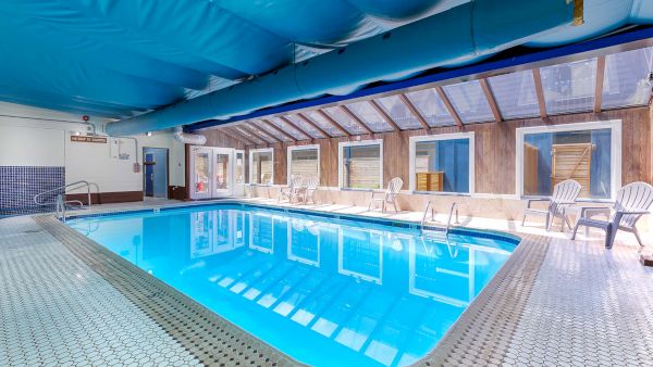 Indoor swimming pool with blue water, tiled deck, a large blue canopy overhead, and several white lounge chairs along the walls.